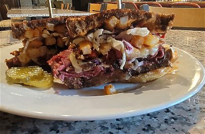 Layered sandwich with meat, coleslaw, and pickles on a plate